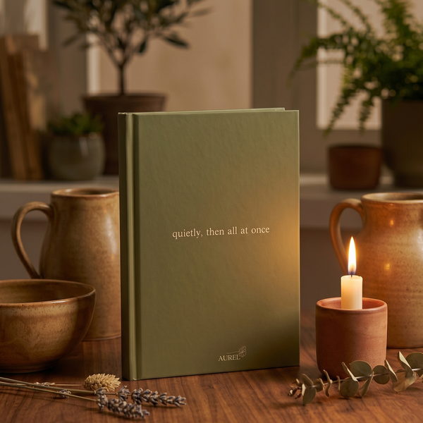 Olive green AUREL journal standing by candlelight among stoneware mugs and eucalyptus